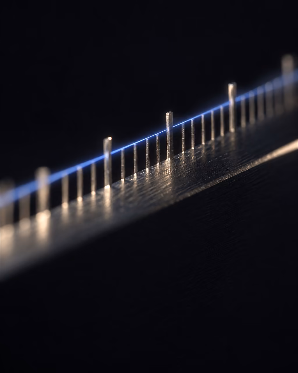 A blue light thread running along a row of small metal tick marks, like a measuring instrument.